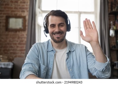 Happy handsome millennial man in wireless headphones video call screen portrait. Businessman, freelance employee, adult student, blogger looking at camera, smiling, waving hand hello. Indoor head - Powered by Shutterstock