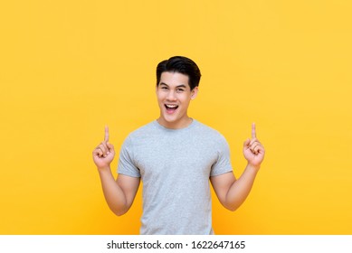Happy Handsome Smiling Young Asian Man With Hands Poiting Up To Empty Space Above