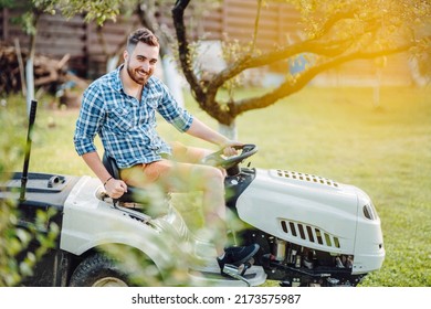 happy handsome worker using ride-on tractor lawn mower