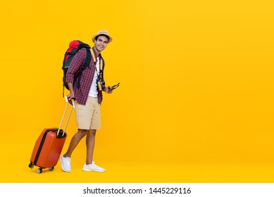 Happy Handsome Young Asian Man With Luggage Ready To Travel For His Holidays Isolated On Yellow Studio Background With Copy Space