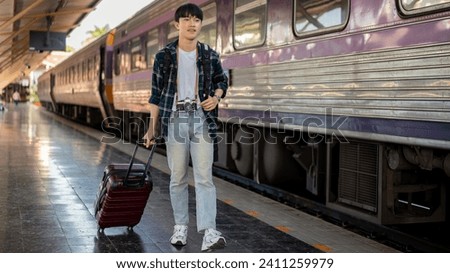 A happy, handsome young Asian man with a backpack and a luggage catching the train at a railway station, walking on a platform, travel somewhere by a train.