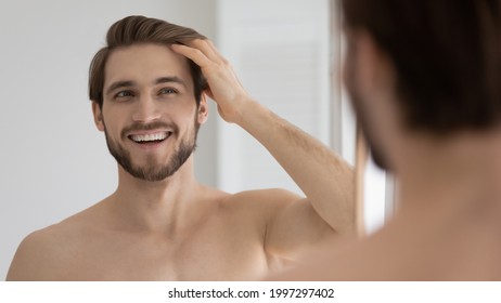 Happy handsome young guy combing smooth brown hair with fingers at mirror in bathroom, looking at reflection with toothy smile. Man satisfied with haircare cosmetic product, enjoying bath routine - Powered by Shutterstock