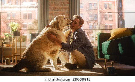 Happy Handsome Young Man Play with His Dog at Home, Gorgeous Golden Retriever. Attractive Man Sitting on a Floor Teasing, Petting and Scratching a Funny Dog, Have Fun in the Stylish Apartment. - Powered by Shutterstock