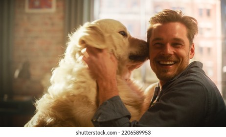 Happy Handsome Young Man Play With His Dog At Home, Gorgeous Golden Retriever. Attractive Man Sitting On A Floor. Excited Dog Licking The Owner That Teases The Pet. Have Fun In The Stylish Apartment.