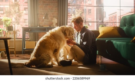 Happy Handsome Young Man Play With His Dog At Home, Gorgeous Golden Retriever. Attractive Man Sitting On A Floor Teasing, Petting And Scratching An Excited Dog, Have Fun In The Stylish Apartment.