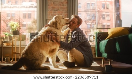 Happy Handsome Young Man Play with His Dog at Home, Gorgeous Golden Retriever. Attractive Man Sitting on a Floor Teasing, Petting and Scratching a Funny Dog, Have Fun in the Stylish Apartment.