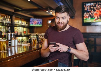 Happy handsome young man sitting and using mobile phone in pub - Powered by Shutterstock