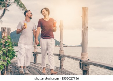 Happy Handsome Young Men, Gay Family In A Tropical Resort With Fruit Necks, LGBT Values, Equal Rights For Everyone. Vacations And Travel.