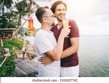 Happy Handsome Young Men, Gay Family In A Tropical Resort With Fruit Necks, LGBT Values, Equal Rights For Everyone. Vacations And Travel.