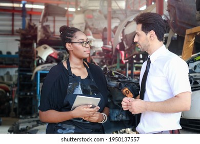 Happy Harmony People At Workplace, White Man And African American Working Together, Checking Product Stock At Auto Spare Parts Store Warehouse With Many Engine Parts As Blurred Background