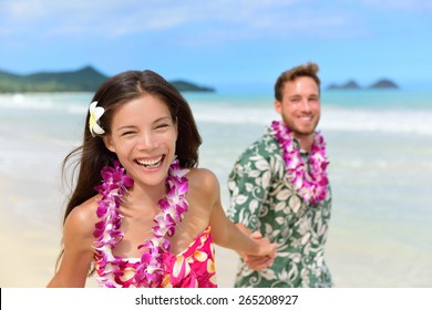 Happy Hawaii Beach Holiday Couple In Aloha Shirt And Dress And Wearing Hawaiian Flower Leis As A Polynesian Culture Tradition For Welcoming Tourists Or For A Wedding Or Honeymoon Vacation.