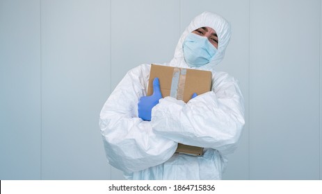 A Happy Health Worker On Protective Suit Hug A Box Of Medical Supplies With His Arms In The Hospital During Pandemic Caused By Covid 19, Coronavirus. The Male Nurse Wears A Surgical Mask.