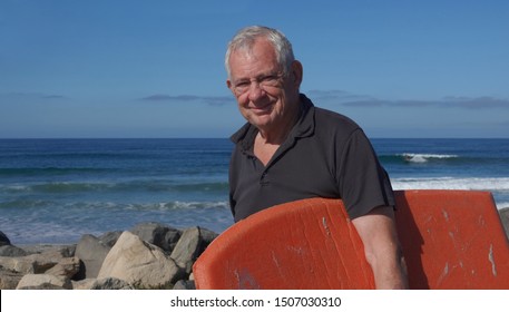 Happy, healthy, active octogenarian (80 year old Caucasian male) on the beach carrying his boogie board - Powered by Shutterstock