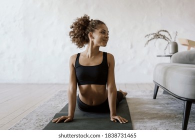 Happy and healthy afro american sporty and fit woman training at home on yoga mat, making sport exercise, stretch upper body, looking aside and smiling against copy space wall on background - Powered by Shutterstock