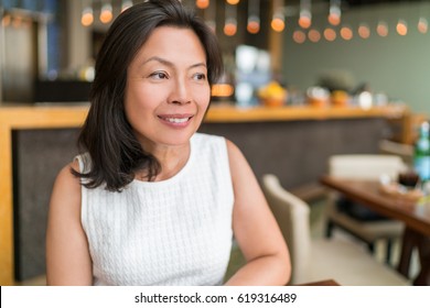 Happy healthy Asian middle-aged business woman relaxing inside restaurant. Beautiful mature Chinese business woman portrait in fancy restaurant. Beauty aging skin care.