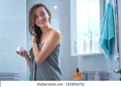 Happy Healthy Attractive Young Brunette Woman In Bath Towel Apply Moisturizing Conditioner To Hair In Bathroom After Shower At Home. Hair Care And Hydration, Female Care