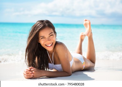 Happy healthy beautiful Asian multiracial woman lying down on sand enjoying sun tanning sunbathing in swimsuit relaxing on Caribbean tropical beach summer vacation. Smiling laughing girl.