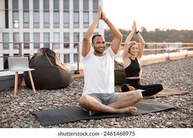 Happy healthy couple meditating on roof on urban background in morning Physically strong man and woman sitting on mats and making yoga with hands raised above their heads. . - Powered by Shutterstock