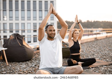 Happy healthy couple meditating on roof on urban background in morning Physically strong man and woman sitting on mats and making yoga with hands raised above their heads. . - Powered by Shutterstock