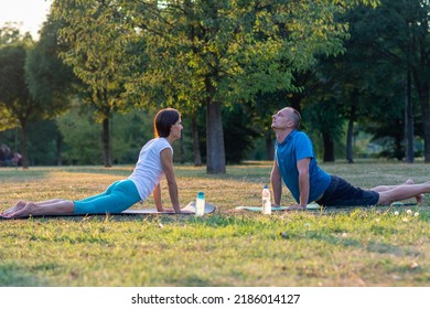 Happy Healthy Couple In Yoga Position. Meditation Concentration Peaceful Serene Relaxation Concept. Couple Yoga On Green Grass Outdoor. Yoga Class. Joyful Peaceful People Practicing Yoga Outdoors