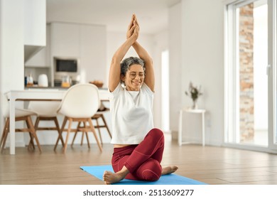 Happy healthy fit mature woman practicing yoga doing exercises sitting on mat at home interior. Sporty mindful older middle aged lady in her 50s stretching body with eyes closed in house living room. - Powered by Shutterstock