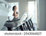 Happy healthy hispanic woman practicing a cardio exercise by running and walking on treadmill machine in fitness and using fitness tracker or smartwatch to track workout progress.