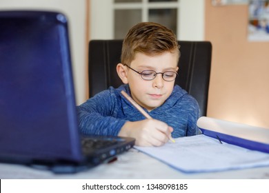 Happy Healthy Kid Boy With Glasses Making School Homework At Home With Notebook. Interested Child Writing Essay With Helping Of Internet. Concetrated Schoolchildren Concept