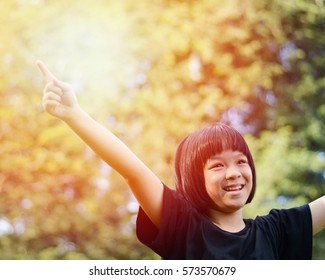 Happy healthy little Asia child pointing index finger into sky in the park on warm summer day during school holidays.Asian Kid girl arms open smiling outside field. Nature parks outdoor concept.  - Powered by Shutterstock