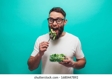 Happy Healthy Man Eating Salad Wearing White T-shirt Isolated Over Blue Background. Healthy Lifestyle Concept