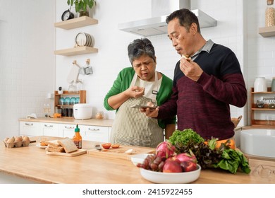 Happy healthy mature older family having breakfast at home. Wife and husband use smartphone during eating sandwich in kitchen together - Powered by Shutterstock