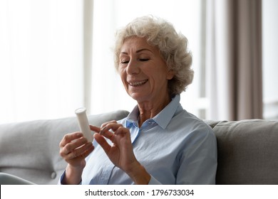 Happy Healthy Middle Aged Grey Haired Woman Holding Medicine Bottle, Reading Instruction For Taking Vitamins. Smiling Retired Granny Examining Pills Label On Complex Supplements Package At Home.