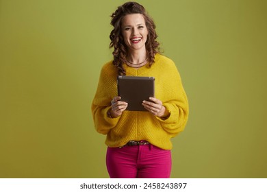 happy healthy middle aged woman isolated on green background in yellow sweater using tablet PC. - Powered by Shutterstock