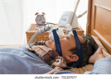 Happy and healthy senior man wearing cpap mask sleeping smoothly without snoring on his back with blurred CPAP machine in background.Obstructive sleep apnea therapy,close up  side view.
