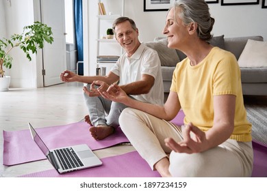 Happy Healthy Senior Older 60s Couple Having Fun Learning To Meditate, Watching Live Online Tv Yoga Class Tutorial On Laptop Computer At Home Doing Virtual Training Fitness Workout Sport Exercises.