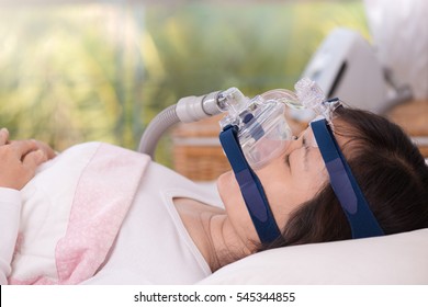  
Happy And Healthy Senior Woman Wearing Cpap Mask Sleeping Smoothly Without Snoring On Her Back With Blurred CPAP Machine In Background.Obstructive Sleep Apnea Therapy ,close Up  Side View.