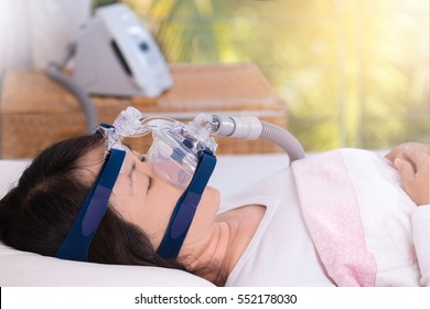 Happy And Healthy Senior Woman Wearing Cpap Mask Sleeping Smoothly Without Snoring On Her Back With Blurred CPAP Machine In Background.Obstructive Sleep Apnea Therapy,close Up  Side View.