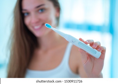 Happy healthy smiling woman with ultrasonic electric brush in bathroom at home. Dental hygiene and teeth care