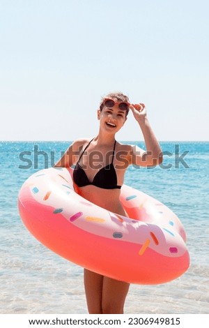 happy healthy woman in black bikini on the ocean coast holding pink inflatable ring. Summer holidays and vacation concept.