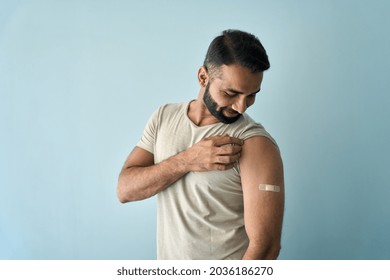 Happy Healthy Young Indian Man Showing Bandage Plaster On Arm Shoulder After Getting Vaccination Standing On Background. Vaccine And People Inoculation In India, Immunity For Covid Prevention.