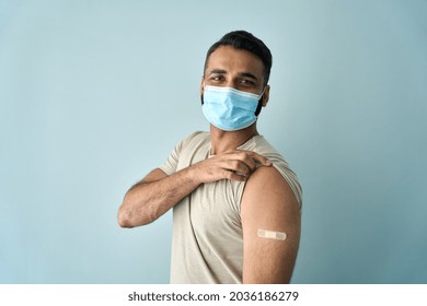 Happy Healthy Young Indian Man Wearing Face Mask Showing Bandage Plaster On Arm Shoulder After Getting Vaccination. Vaccine And People Inoculation, Immunity For Covid Prevention Concept. Portrait