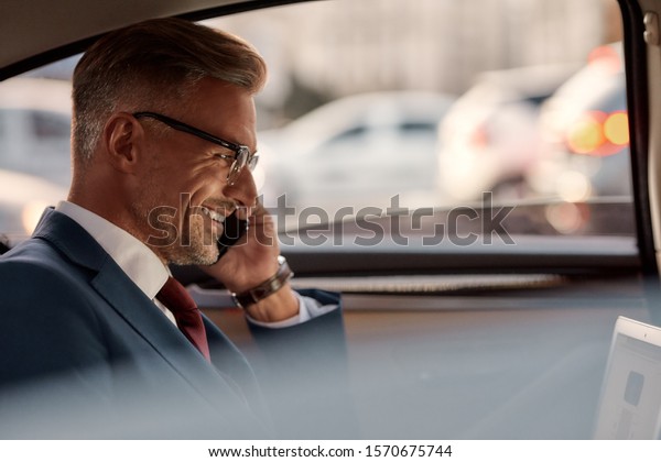 So happy to hear you. Side\
view of mature businessman sitting in the car and talking by the\
phone