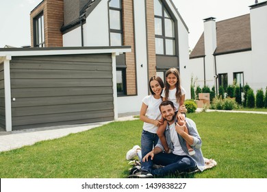 Happy heteroseksual family sitting on grass near their new house. Family sitting on lawn, buying new big home .