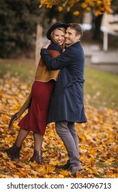 Happy Heterosexual Couple Hugs While Walking At The City Park On The Autumn Day. Handsome Man Hugs His Beautiful Pregnant Wife Outdoors