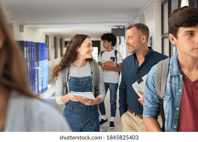 Happy High School Student Talking To Mature Man Professor In Hallway. Senior Man Teacher In Conversation To School Girl In Campus. Helpful Lecturer Explaining Concept To College Student In Corridor.