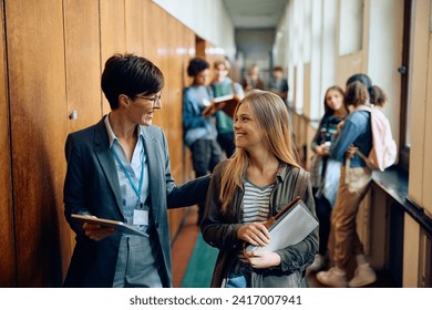 Happy high school teacher talking to her student while walking through the hallway. - Powered by Shutterstock