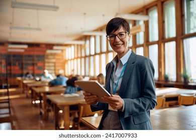 Happy high school teacher using digital tablet in the classroom and looking at camera. Her students are in the background. - Powered by Shutterstock