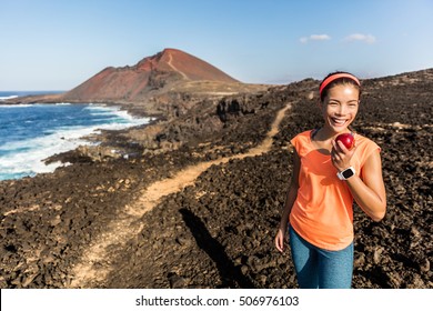 Happy Hiker Hiking On Mountain Trail Path Taking A Break Eating A Healthy Snack - Apple Fruit. Fitness Woman Runner On Trail Running Training Enjoying Organic Food In Mountains Landscape.