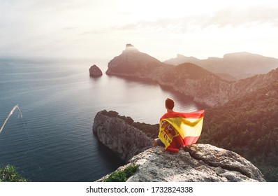 Happy hiker holds a flag of Spain behind her celebrating on Formentor cape to Pollensa high aerial sea view in Mallorca balearic islands - Powered by Shutterstock