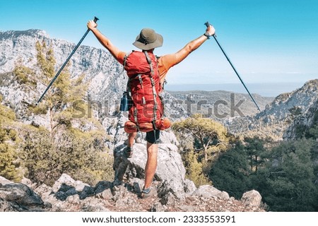 Happy hiker man with trekking backpack and outstretched arms with hiking poles on a rocky cliff during walk on Lycian Way trail in turkish mountains