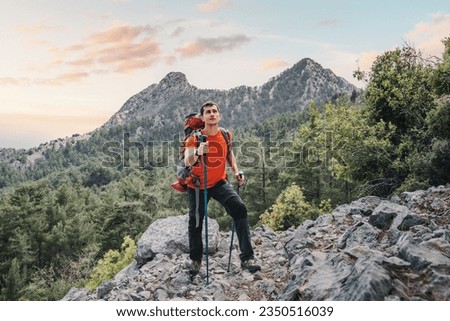 Happy hiker man with trekking backpack and hiking poles on a rocky cliff during walk on Lycian Way trail in turkish mountains